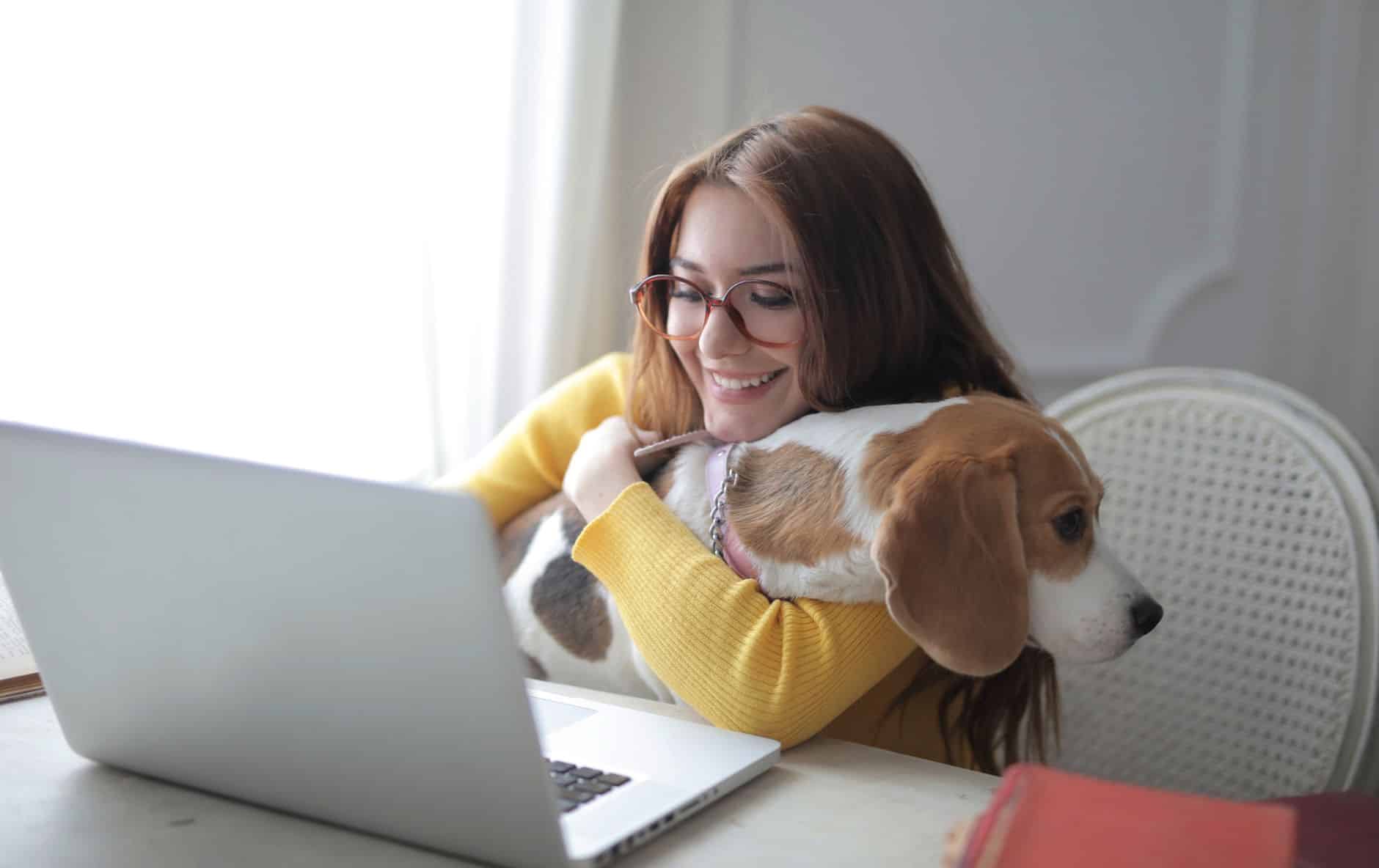 Une femme en visio sur son ordinateur portable à la maison, son beagle blotti contre elle
